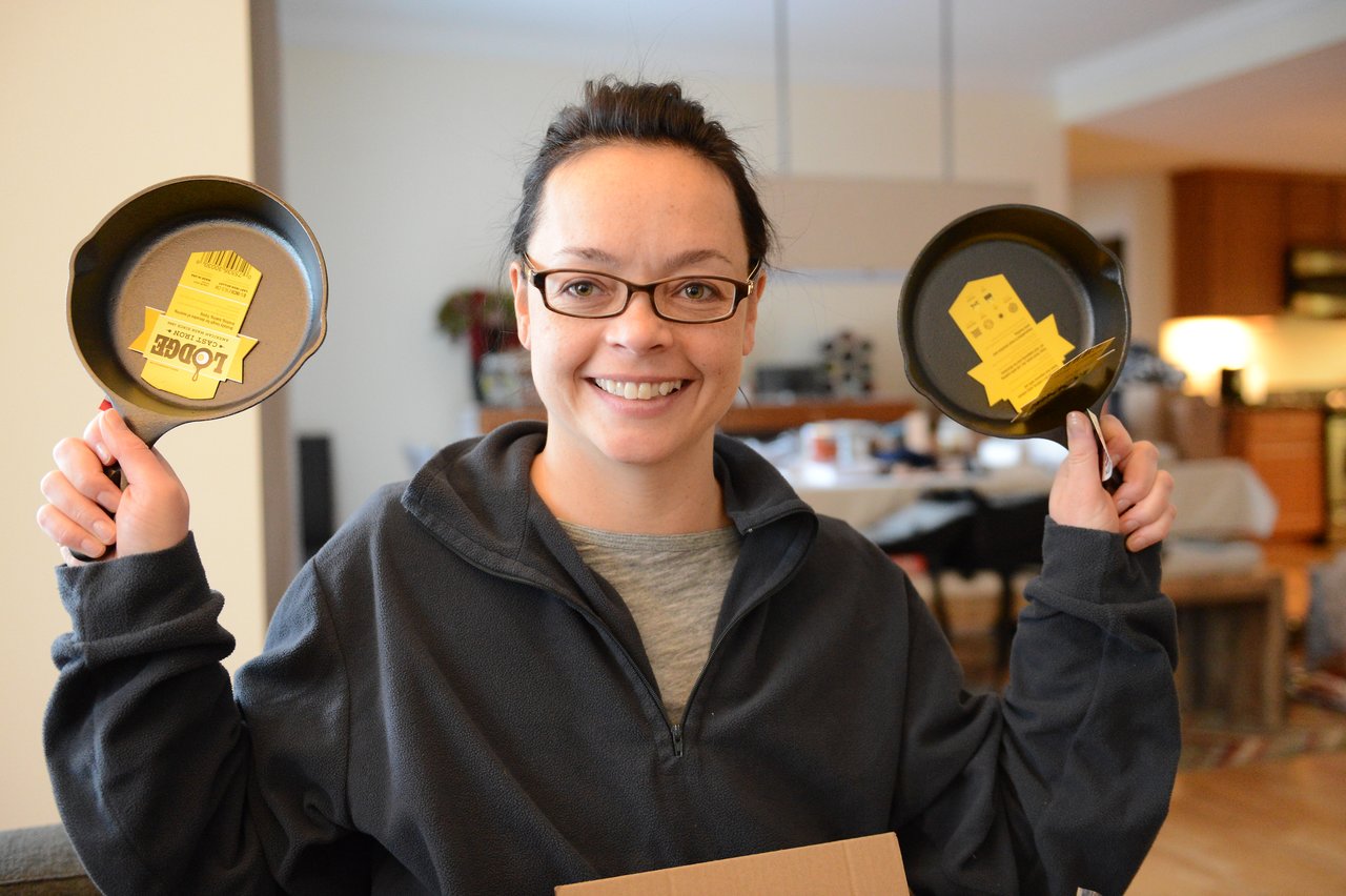 A smiling person holds up two small cast iron skillets with tags, appearing to have just unboxed them.