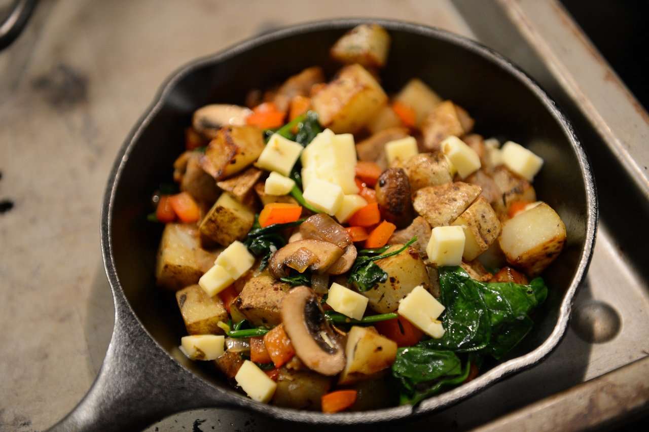 A skillet filled with roasted potatoes, mushrooms, spinach, diced carrots, and small cubes of cheese.