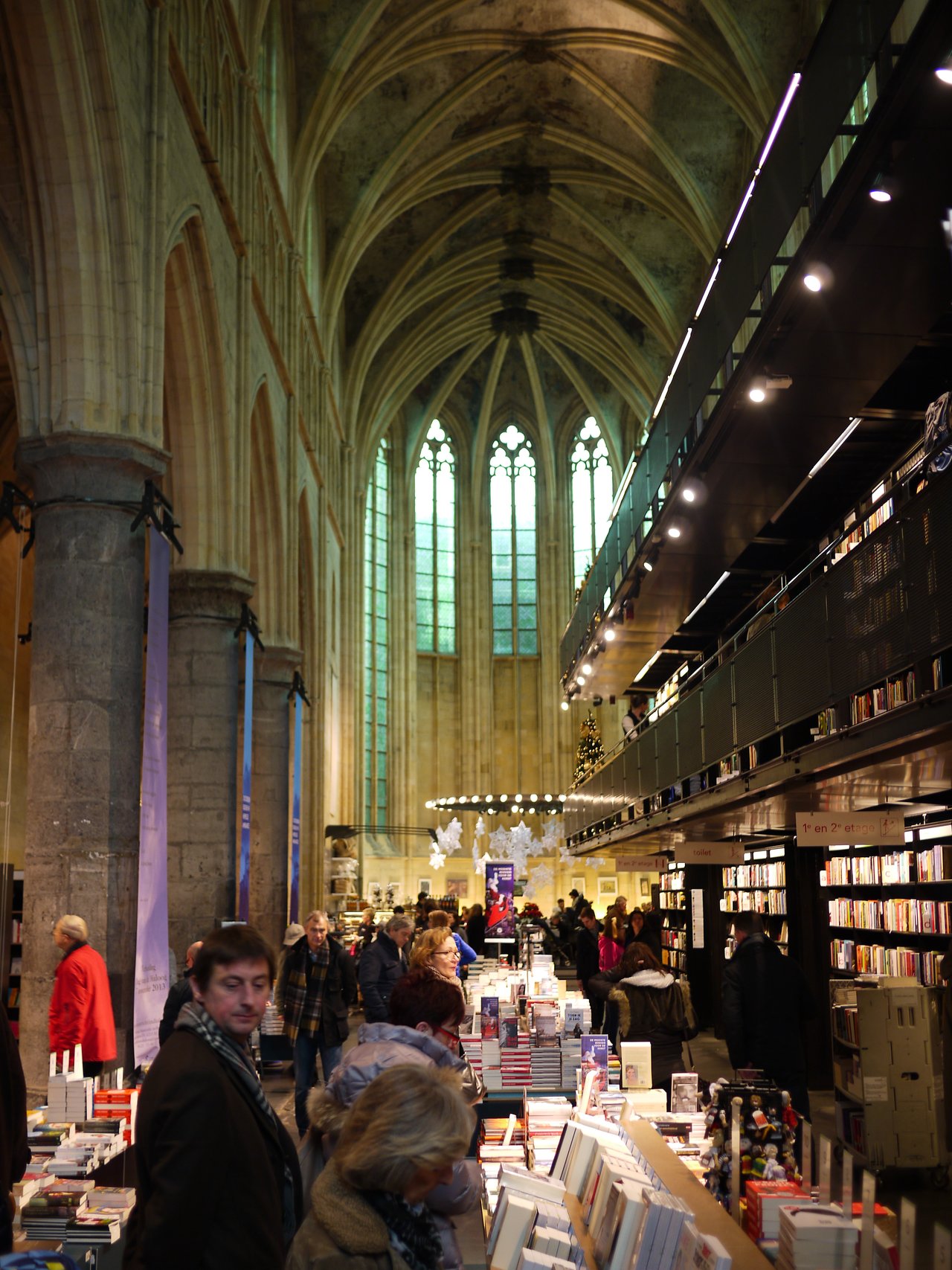 People browsing books inside a bookstore located in a historic church with high ceilings and stained glass windows.