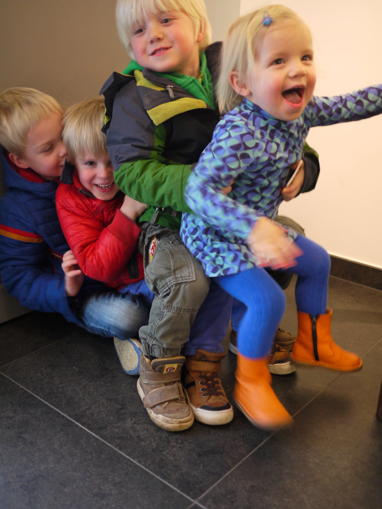 Four children sit closely together, laughing and playing indoors.