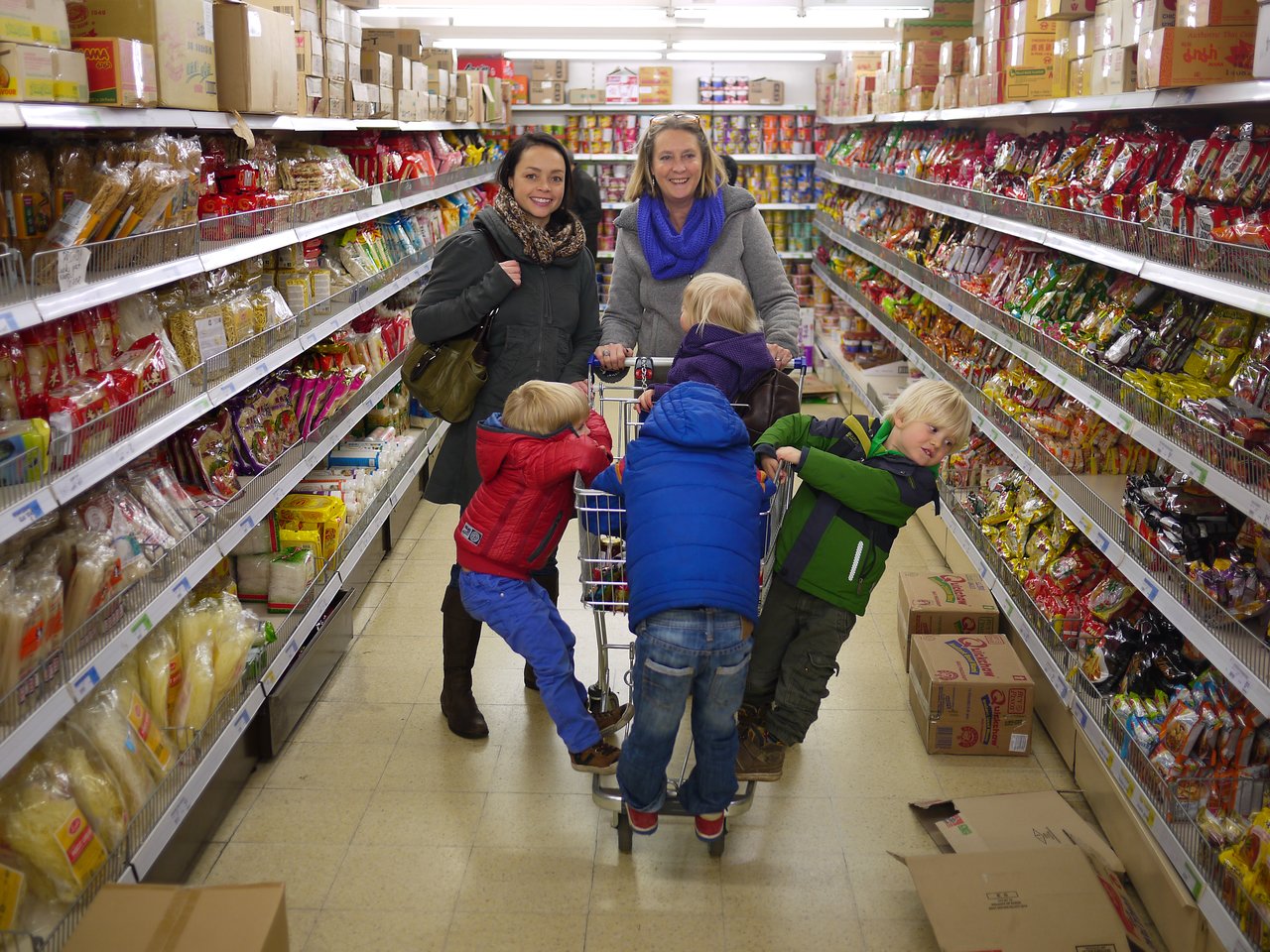 Two women and four children shopping in a Chinese supermarket, with kids playing around a shopping cart.