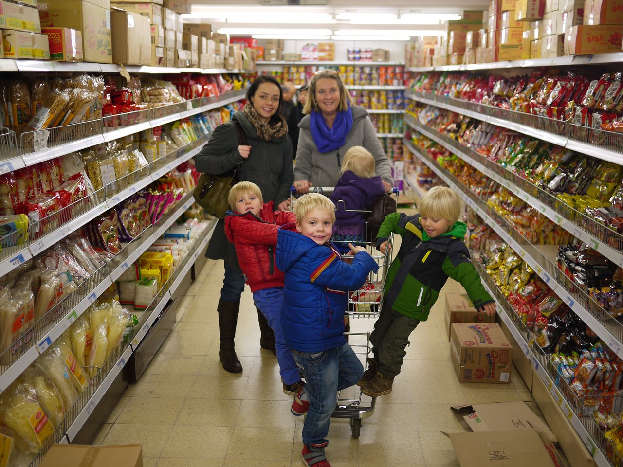 Two women and several children shopping in a Chinese supermarket, with kids playing around a shopping cart.