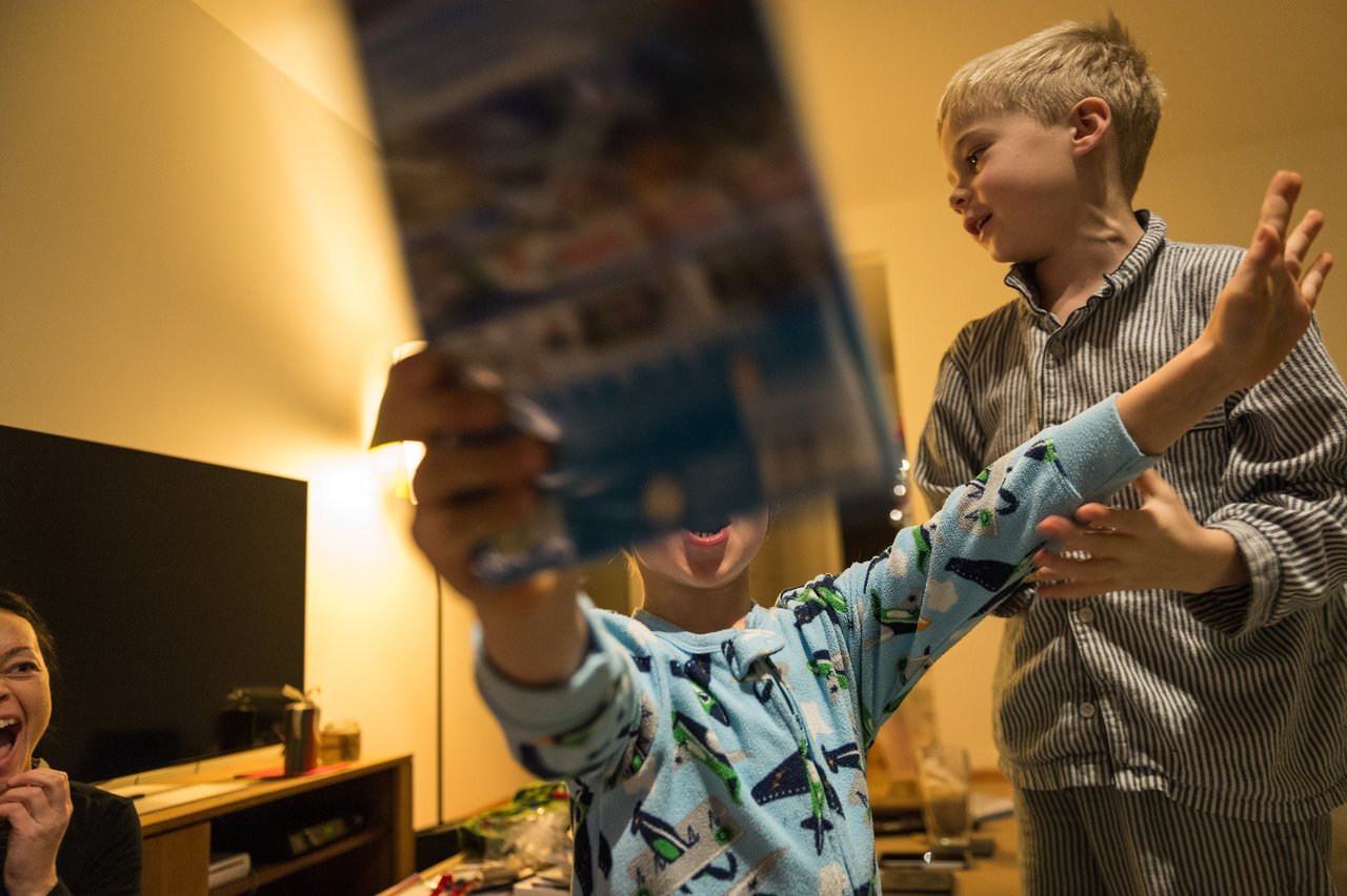 A child excitedly holds up a gift while another child smiles nearby.