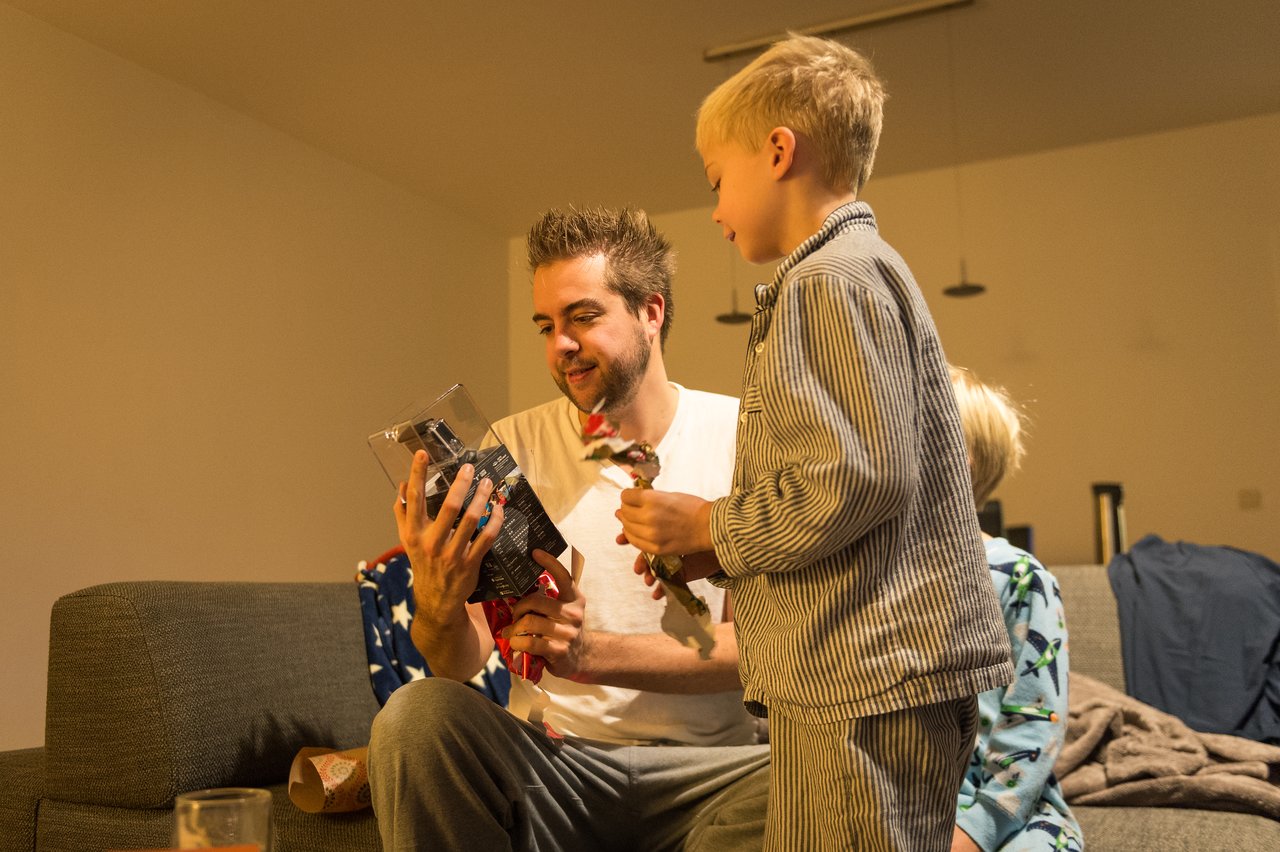 A man and two children open Christmas presents together, examining a toy and its packaging.
