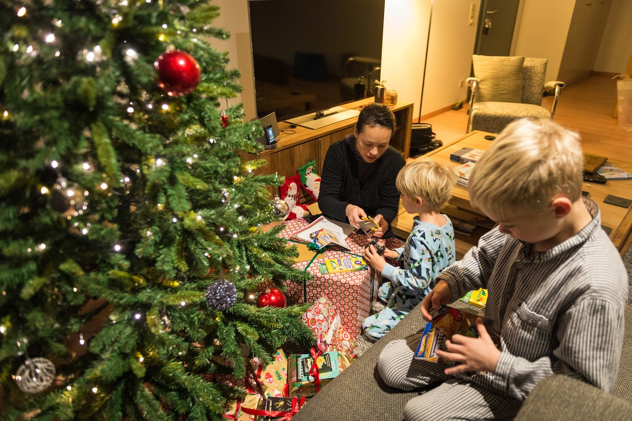 A family sits near a Christmas tree, opening presents and snacks together in a cozy living room.