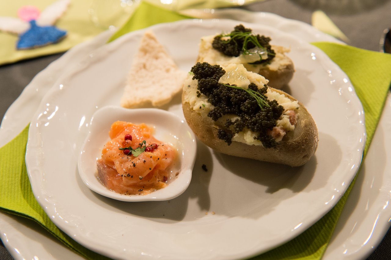 A plate with stuffed potatoes topped with caviar, a small dish of salmon, and a piece of bread.