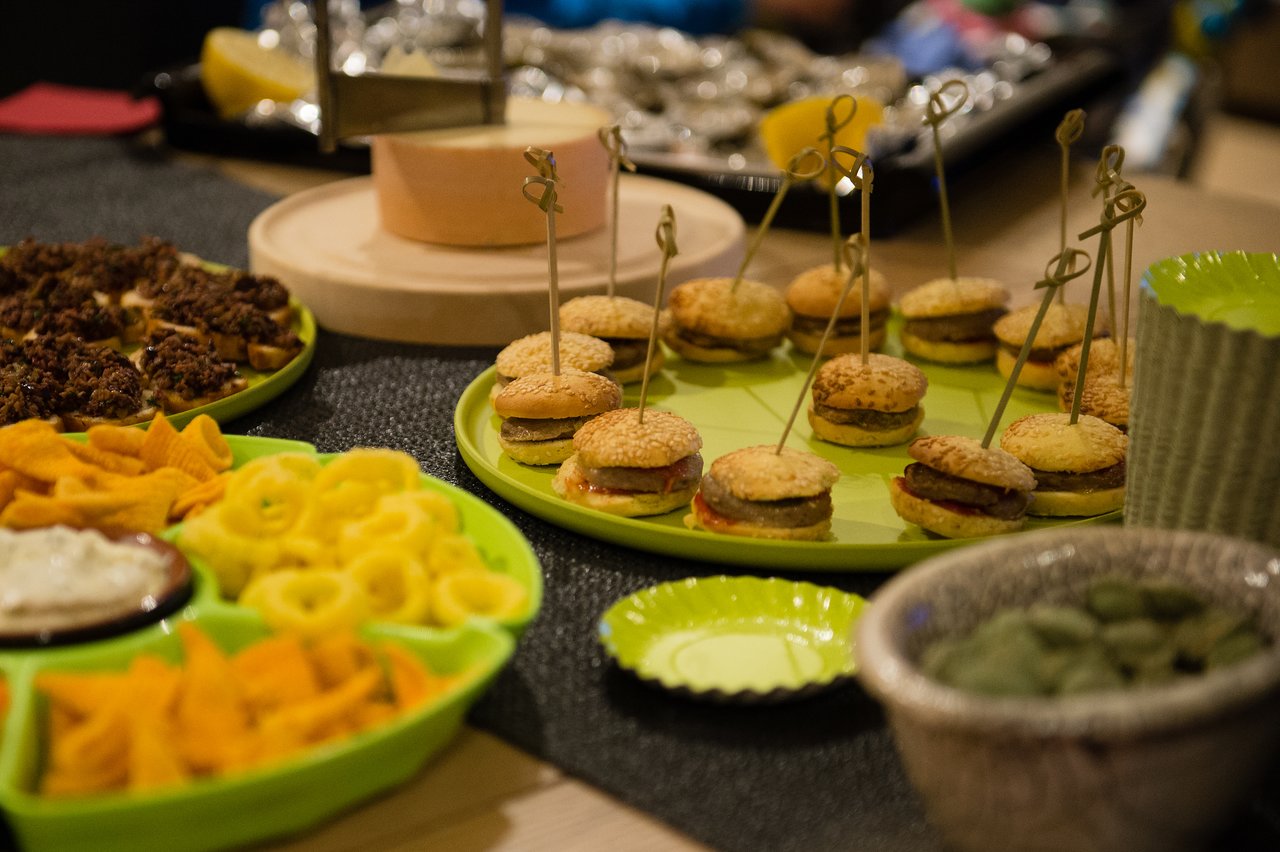 A table with mini burgers on skewers, chips, dip, and other snacks arranged on green plates.