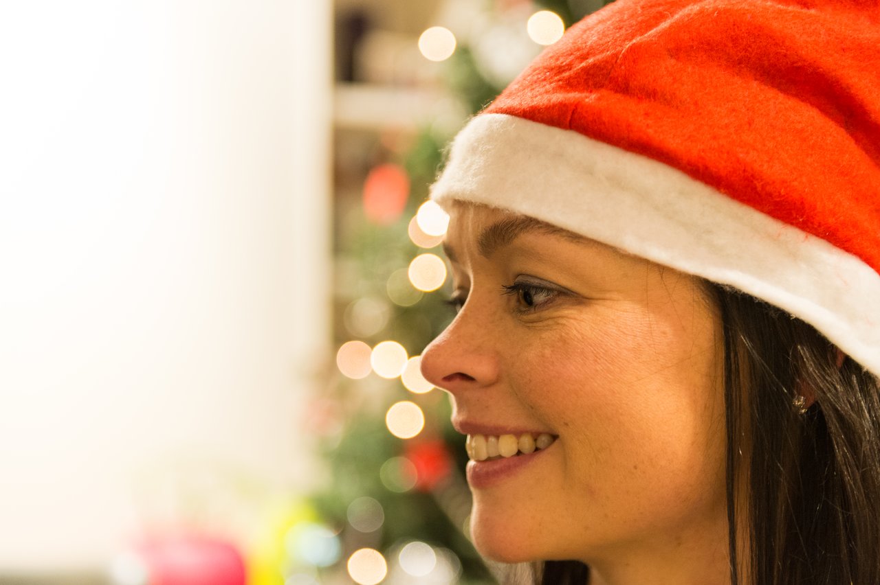 A person wearing a Santa hat smiles, with a decorated Christmas tree in the blurred background.