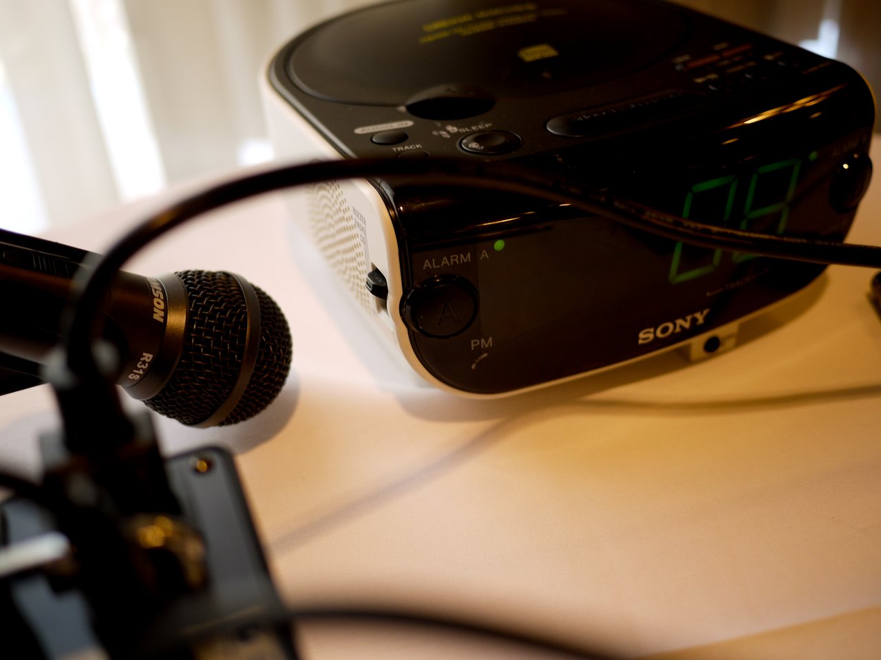 A microphone, audio equipment, and a Sony digital clock radio on a table with cables running across.