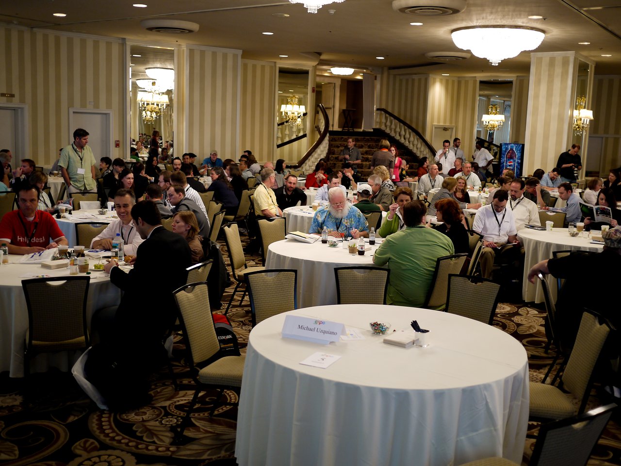 A large group of people seated at round tables in a conference room, engaged in discussions and networking.