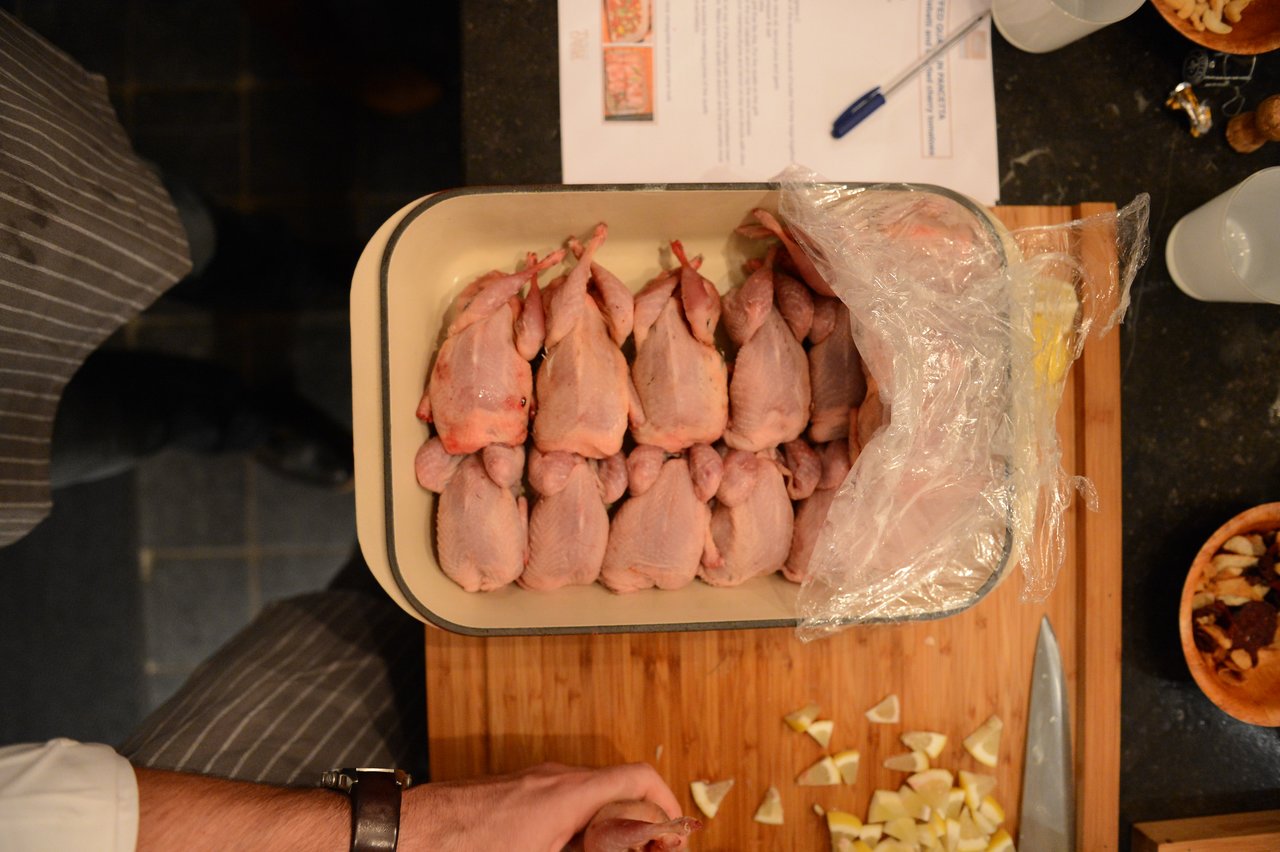 A person in a cooking class holds a tray of raw, plucked quails on a wooden cutting board.