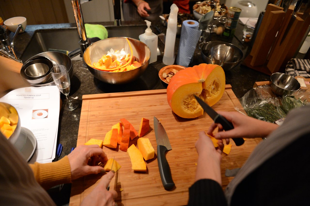 Two people cutting a pumpkin into pieces on a wooden board during a cooking class.