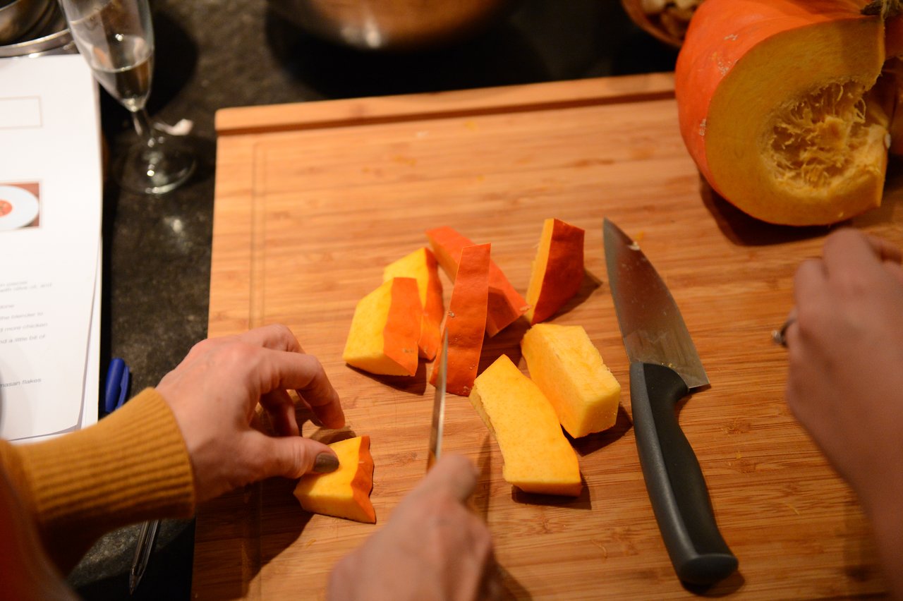 Hands cutting pumpkin into pieces on a wooden cutting board during a cooking class.