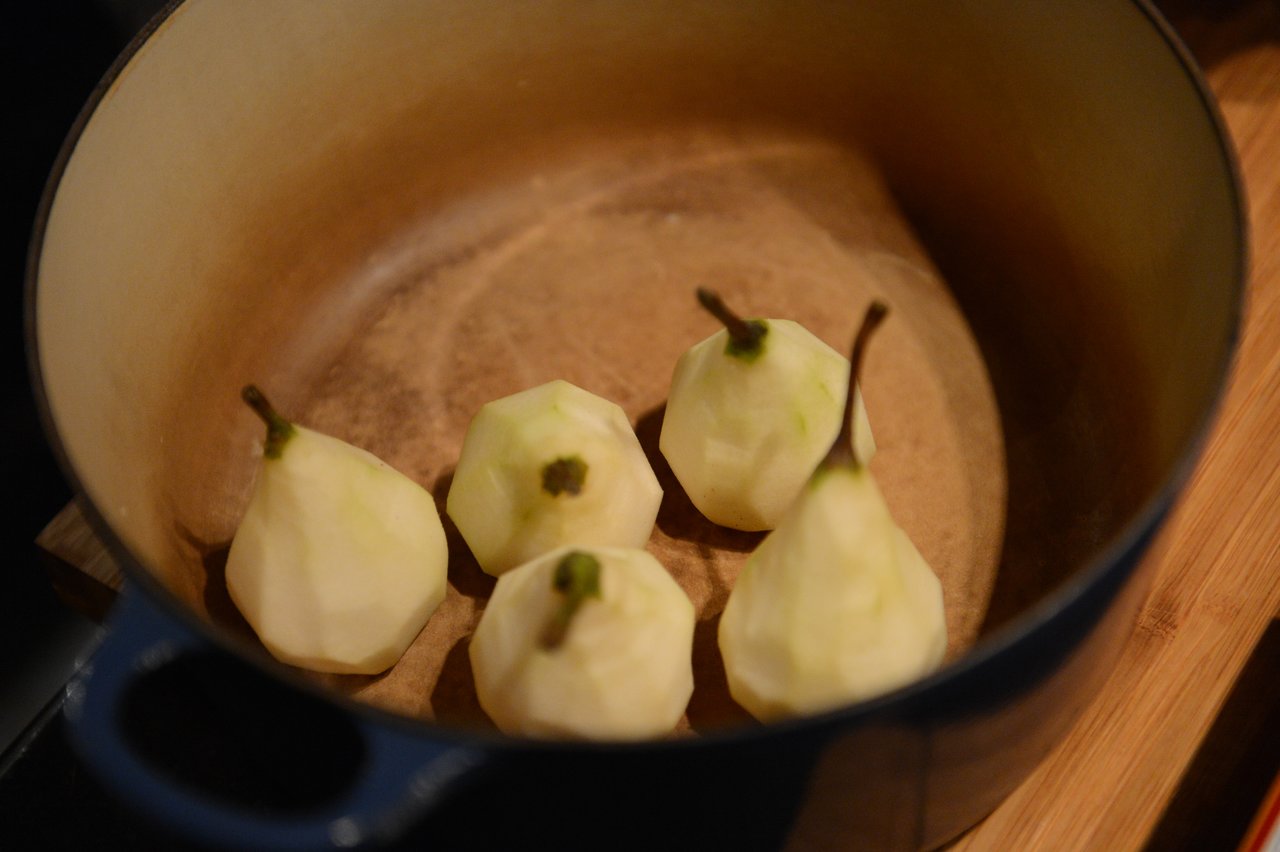 Five peeled pears are placed inside a large pot, ready for cooking.