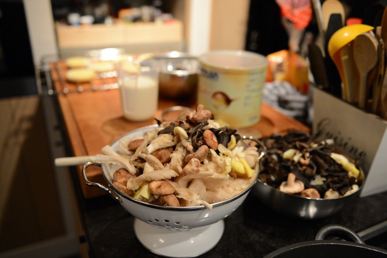 A colander filled with assorted mushrooms sits on a kitchen counter during a cooking class.