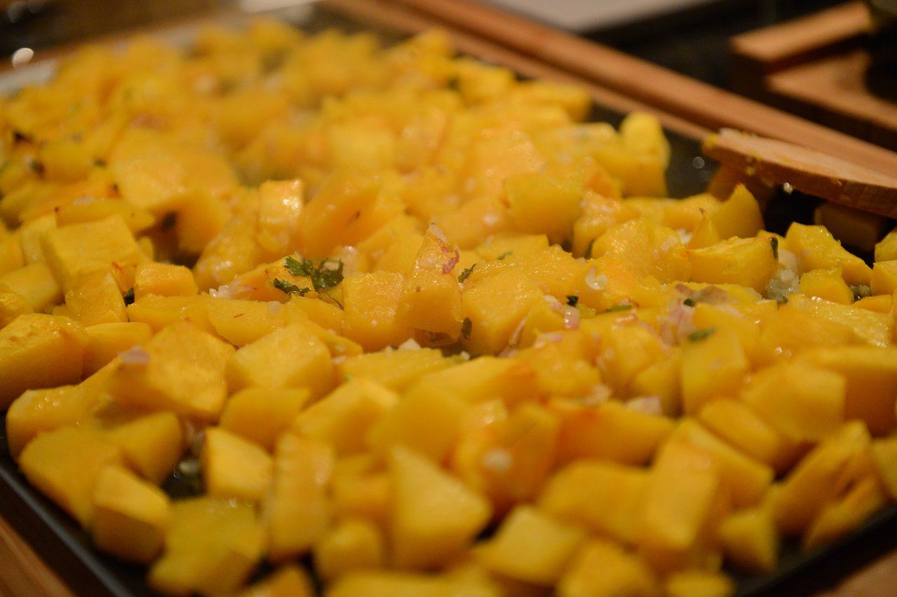 Chopped yellow squash with herbs and onions on a baking tray, prepared during a cooking class.