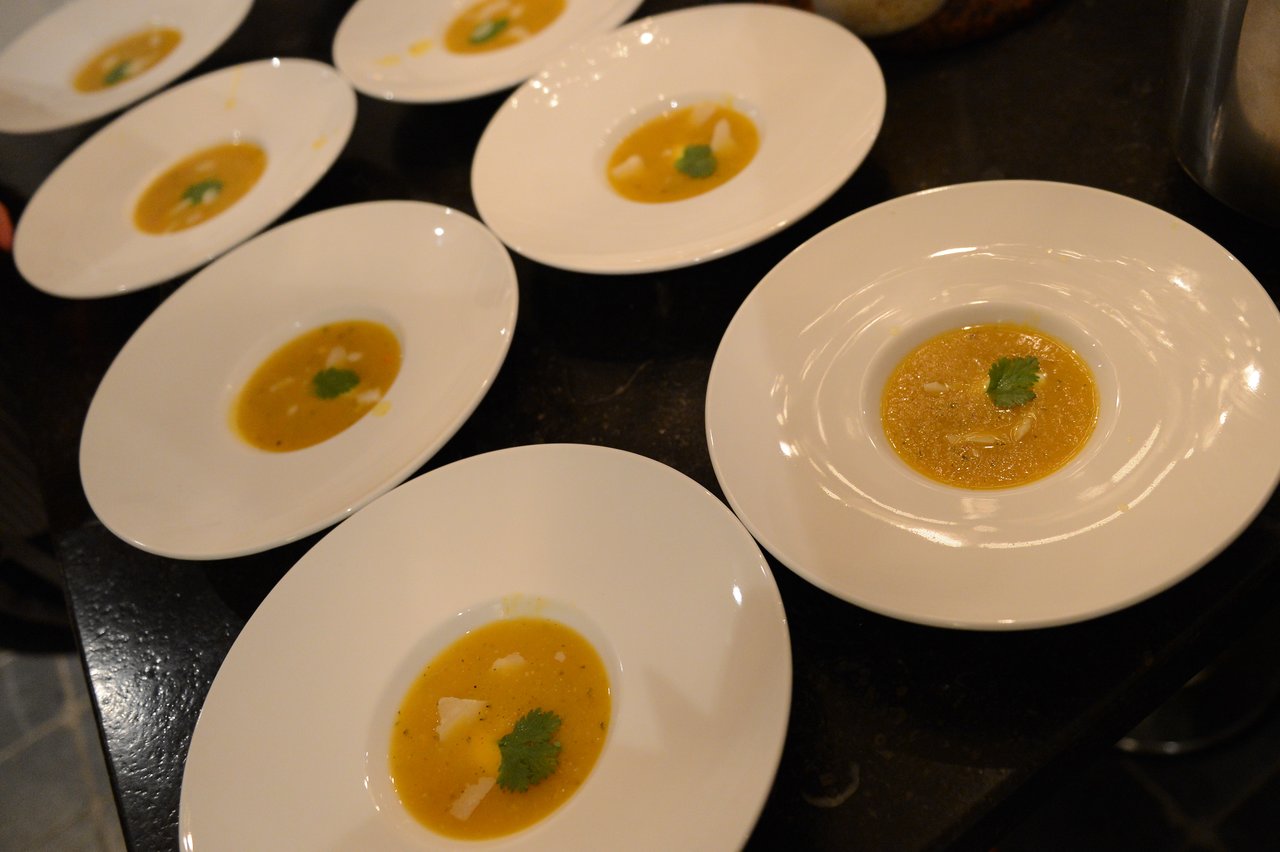 Several white plates with small servings of yellow soup, garnished with cilantro, arranged on a dark countertop.