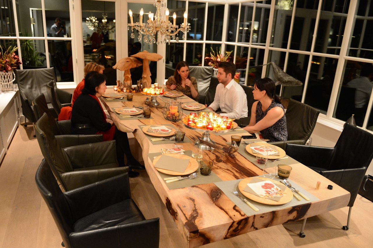 A group of people sits around a decorated dining table, engaged in conversation during a cooking class gathering.