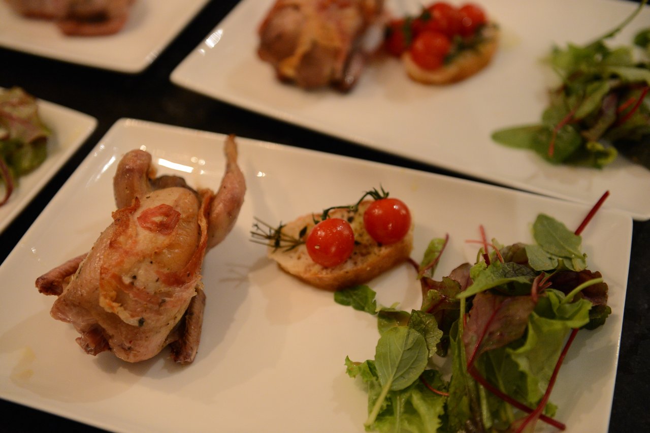A plated dish with roasted quail, toasted bread with cherry tomatoes, and a side of mixed greens.