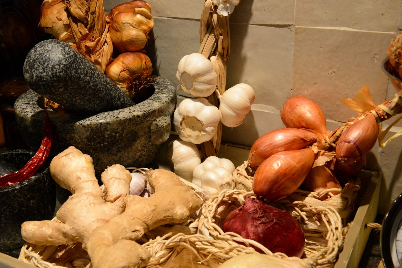 A mortar and pestle surrounded by garlic, onions, ginger, and chili peppers in a cooking class setting.