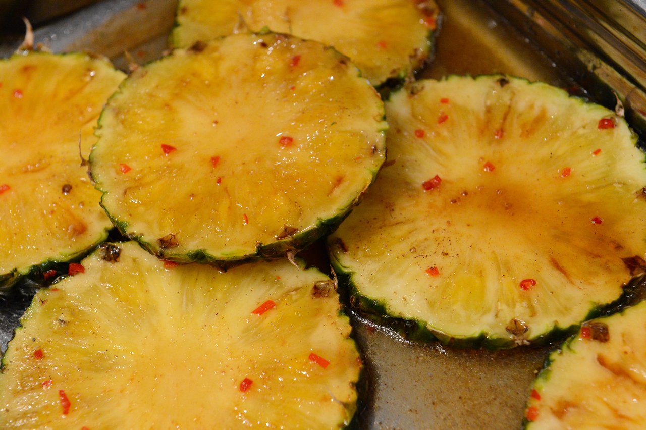 Sliced pineapples marinated with spices and red pepper flakes in a baking dish during a cooking class.