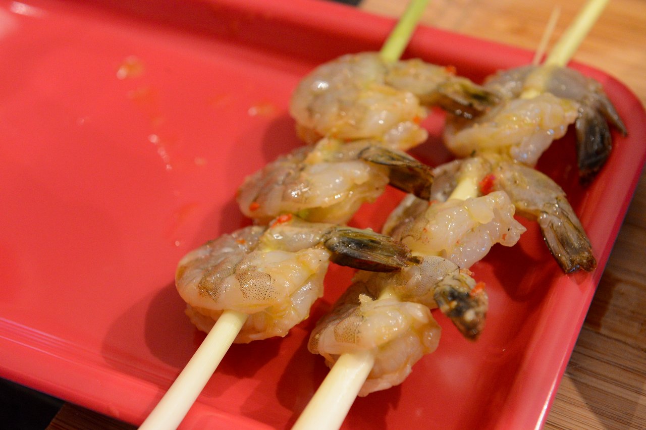Raw shrimp skewered on lemongrass sticks, placed on a red tray, prepared for cooking in a class.