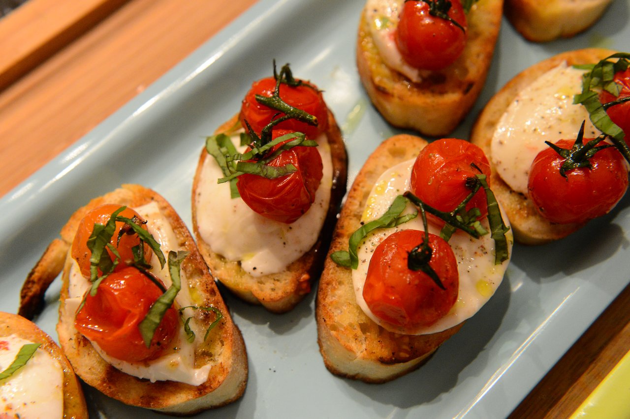Toasted bread with mozzarella, roasted cherry tomatoes, and basil on a blue plate, prepared during a cooking class.