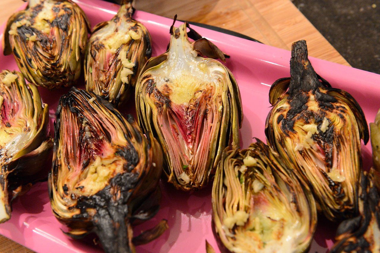 Grilled artichokes with melted butter and seasoning on a pink tray, prepared during a cooking class.