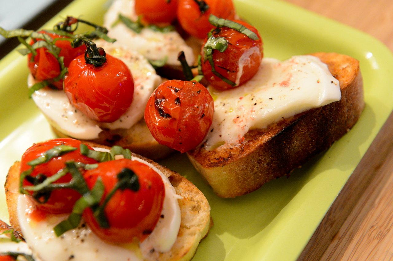 Toasted bread with melted cheese, roasted cherry tomatoes, and fresh basil on a green plate.