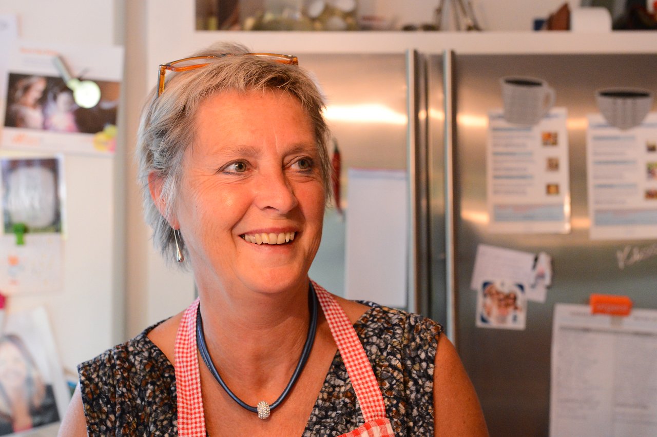 A woman wearing an apron smiles in a kitchen during a cooking class.