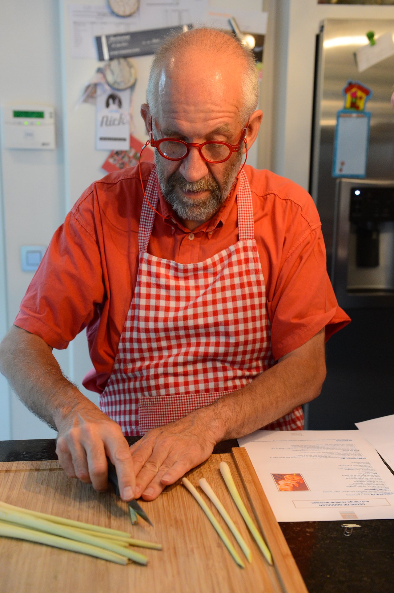 A man in a red checkered apron chops lemongrass on a wooden cutting board during a cooking class.