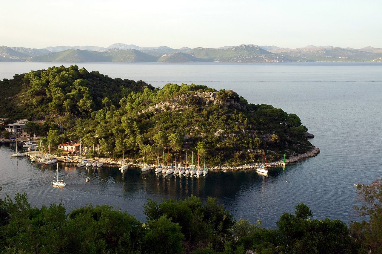 Sailboats docked along the shore of a small bay, surrounded by green hills and calm water.