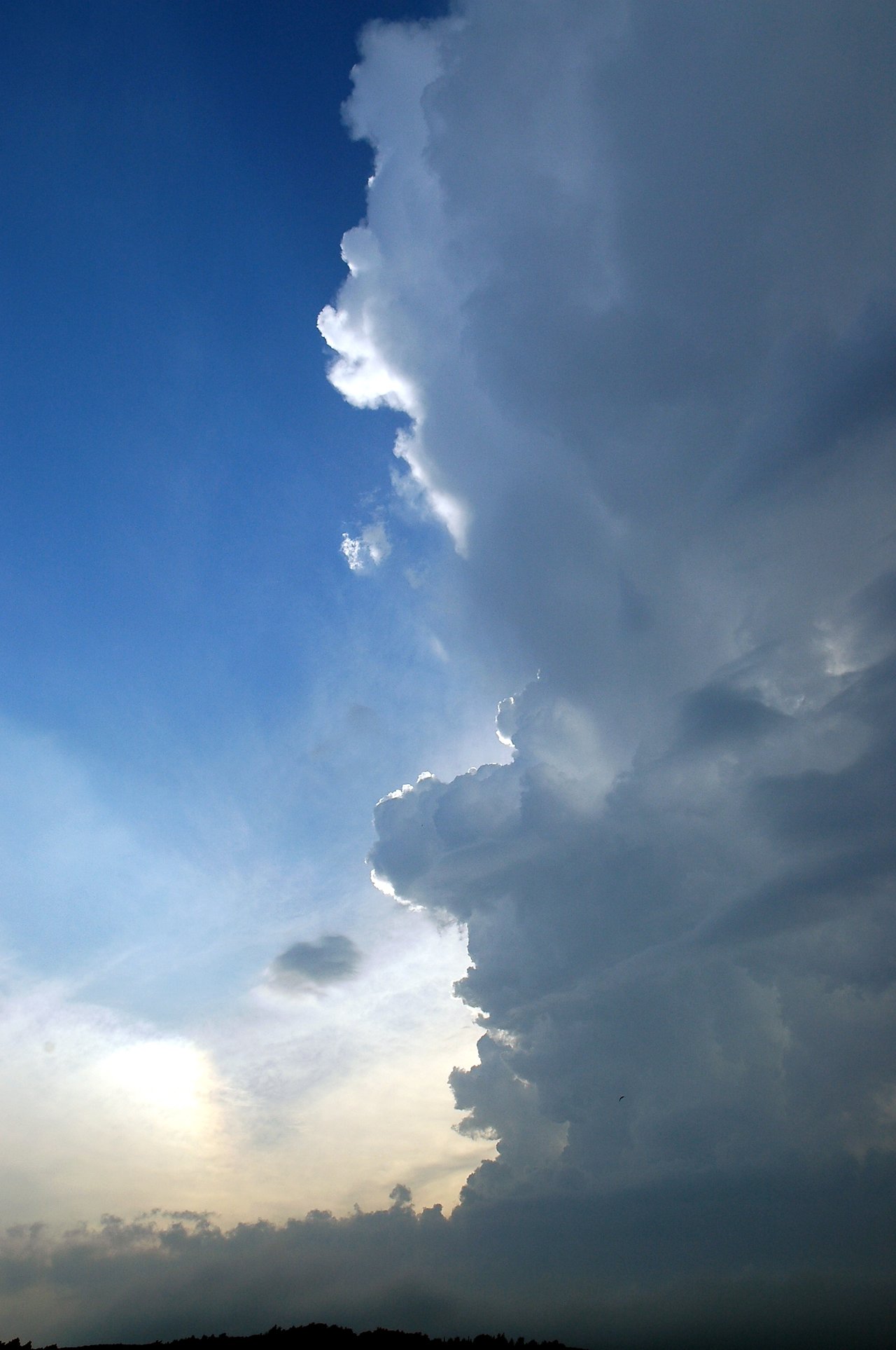 Dark storm clouds build up in the sky, contrasting with the bright blue sky and sunlight near the horizon.
