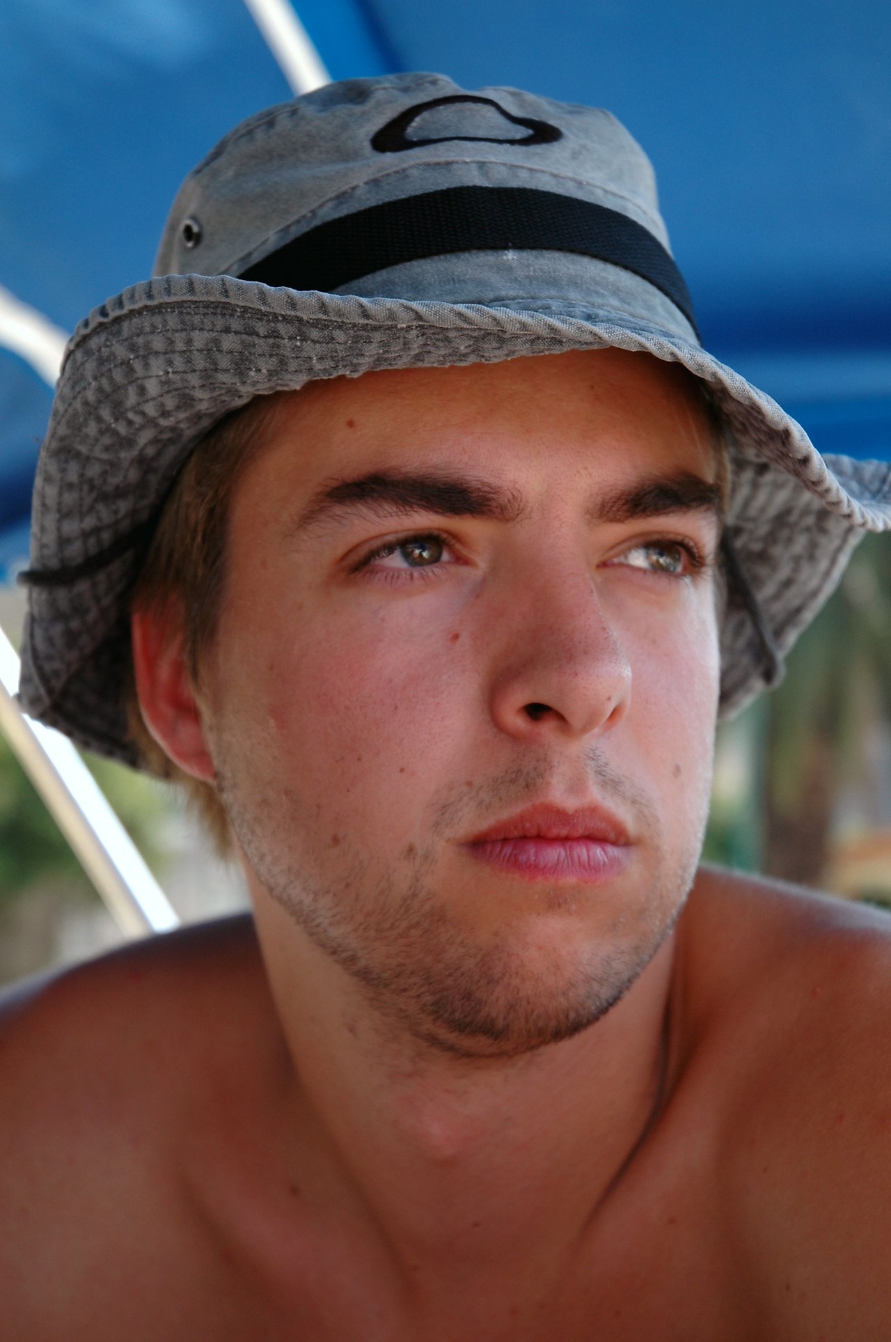 A young man wearing a gray bucket hat looks into the distance under a blue canopy.