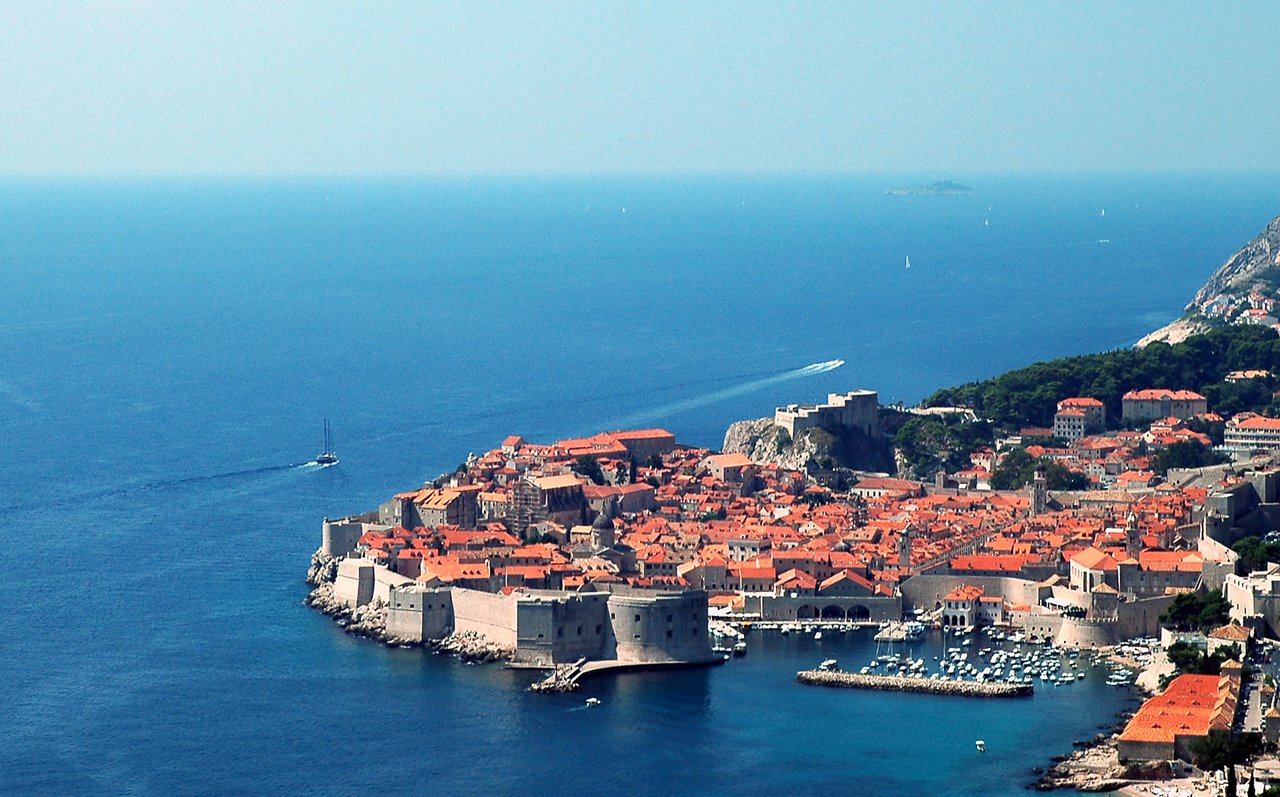 Aerial view of Dubrovnik's old town with stone walls, red rooftops, and boats in the surrounding sea.