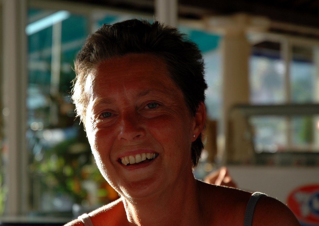 A woman with short hair smiles while sitting outside in natural light.