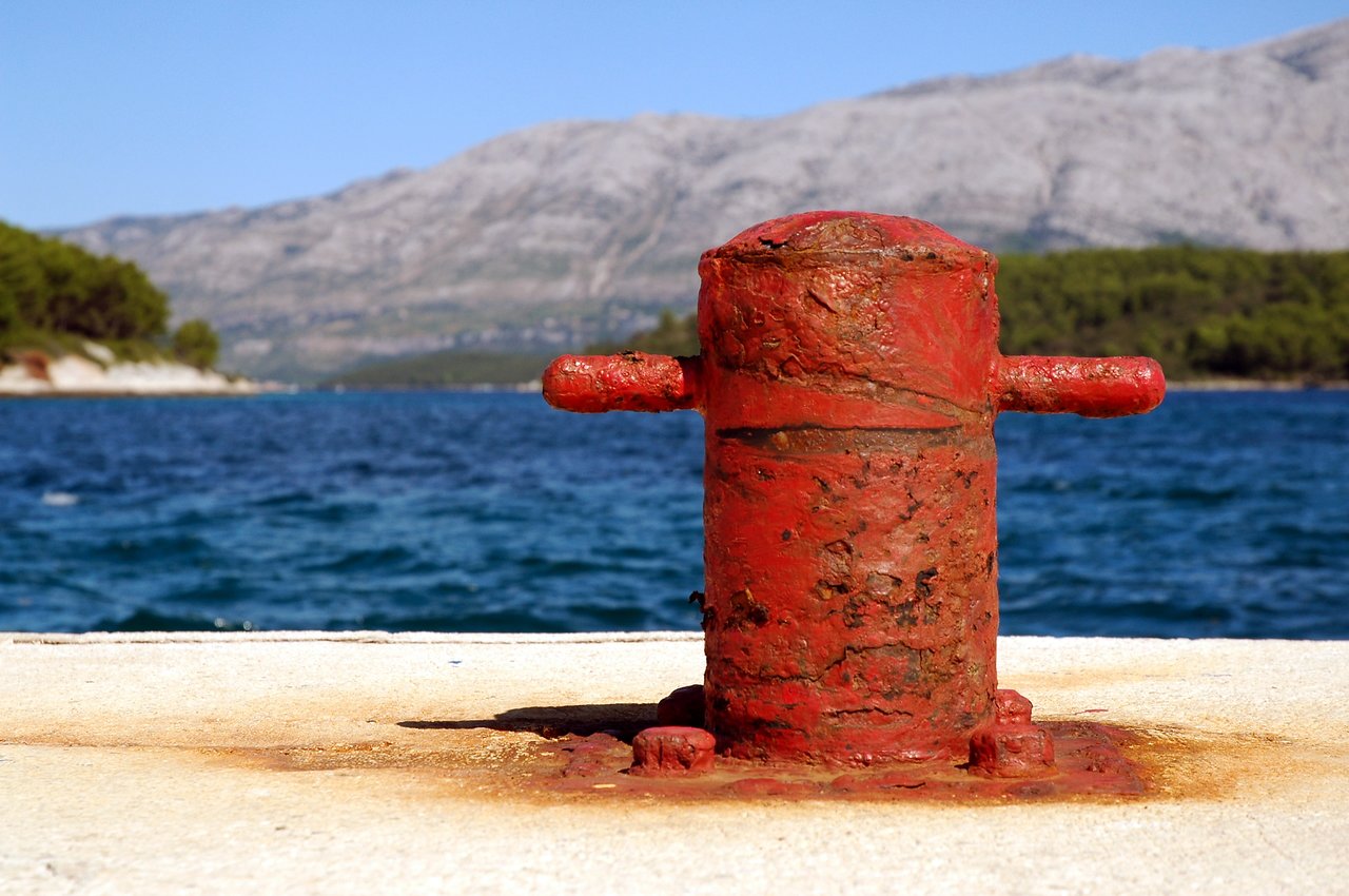 A rusty red mooring bollard on a concrete pier, used for securing boats.
