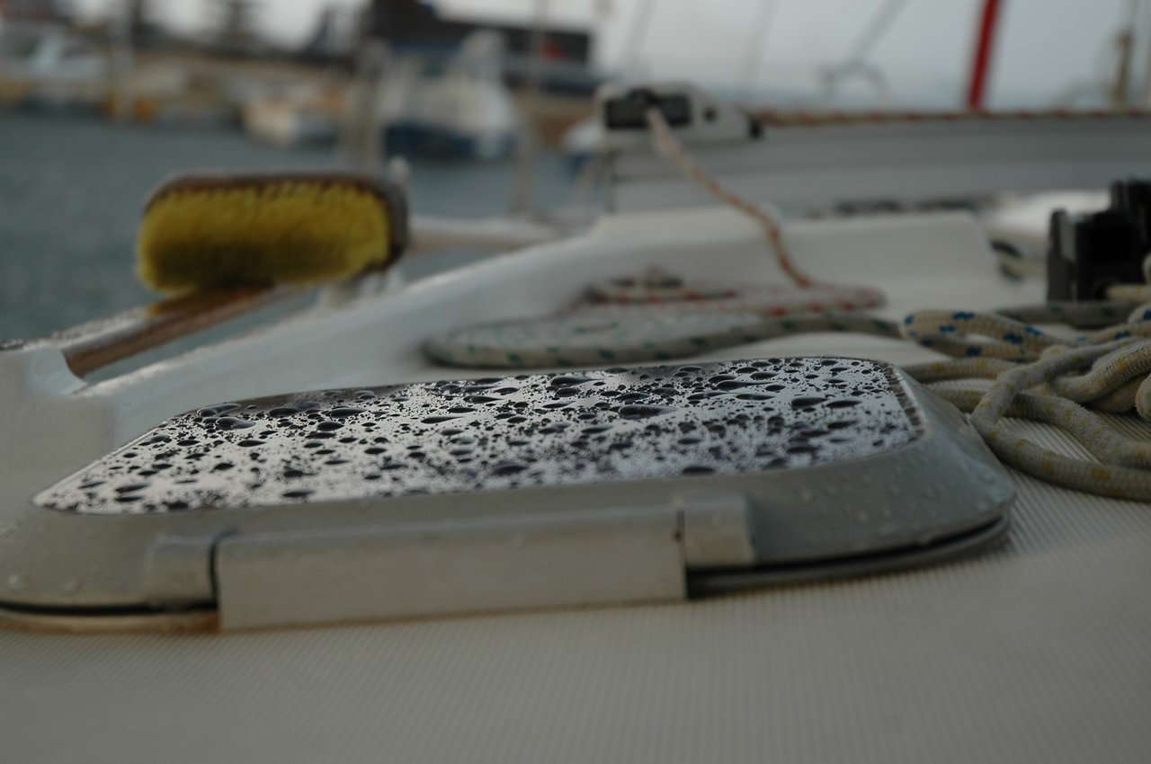 Raindrops on a small boat hatch window, with ropes and a brush in the background.