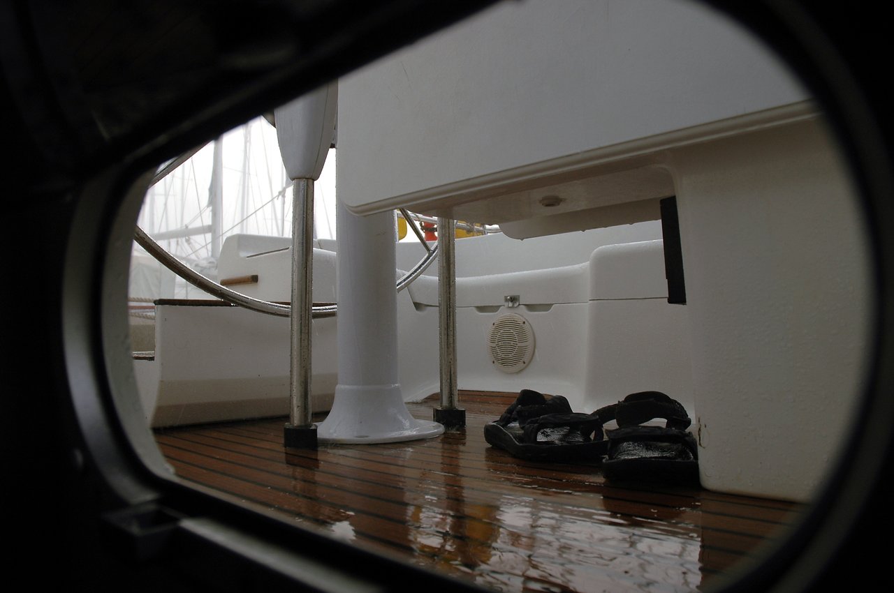 Wet sandals rest on a wooden boat deck, seen through a round opening on a rainy day.