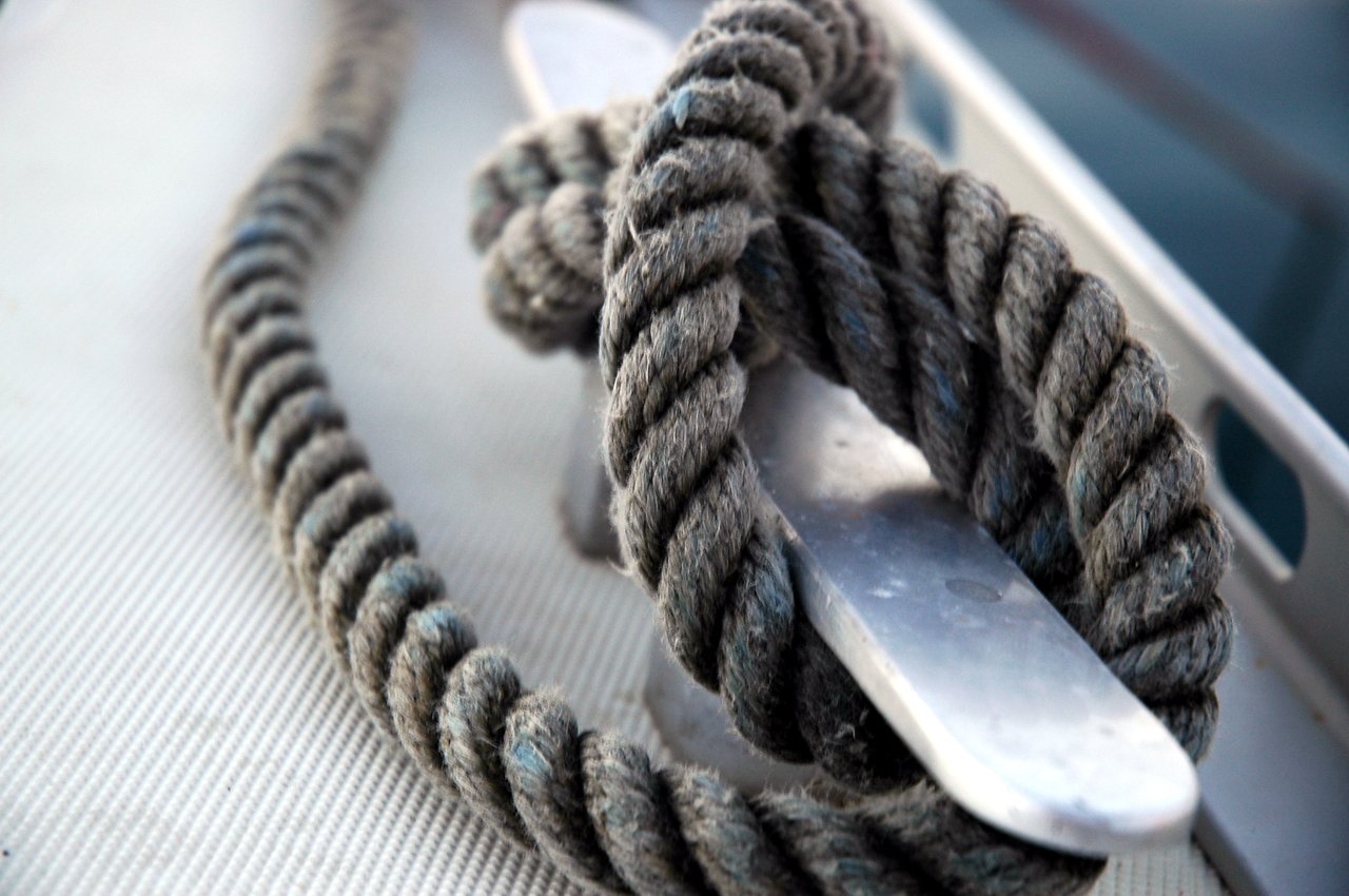 A thick rope is tightly wrapped around a metal cleat on a boat's surface.