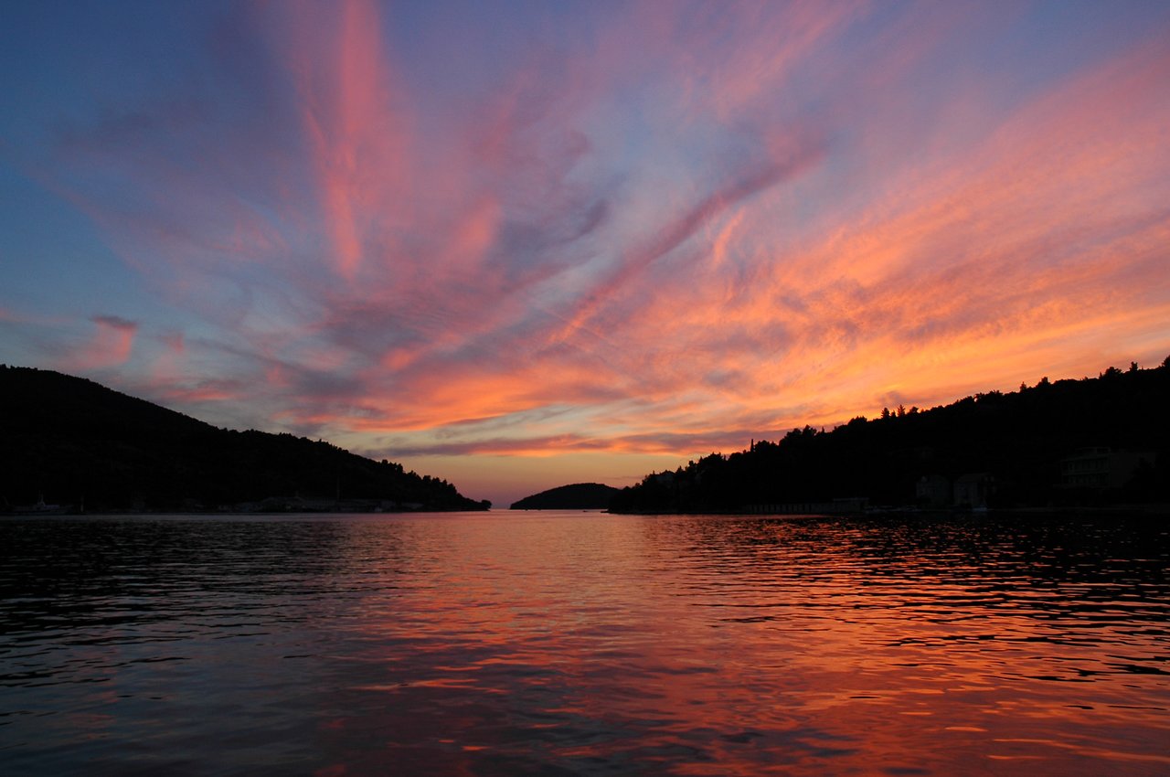The sun sets over calm water, with orange and pink hues reflecting on the surface.
