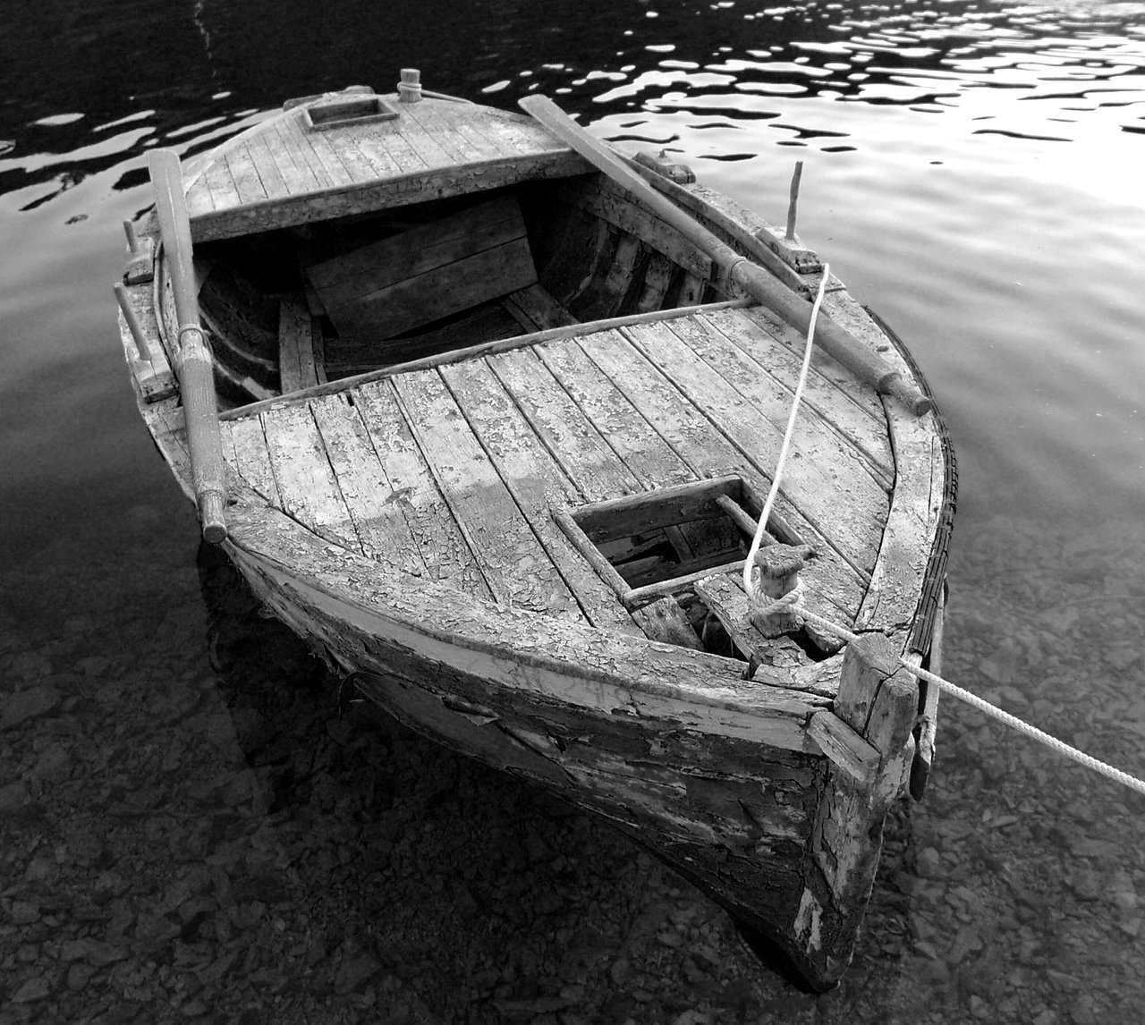 An old wooden boat with oars is tied to a rope, floating on calm, clear water.