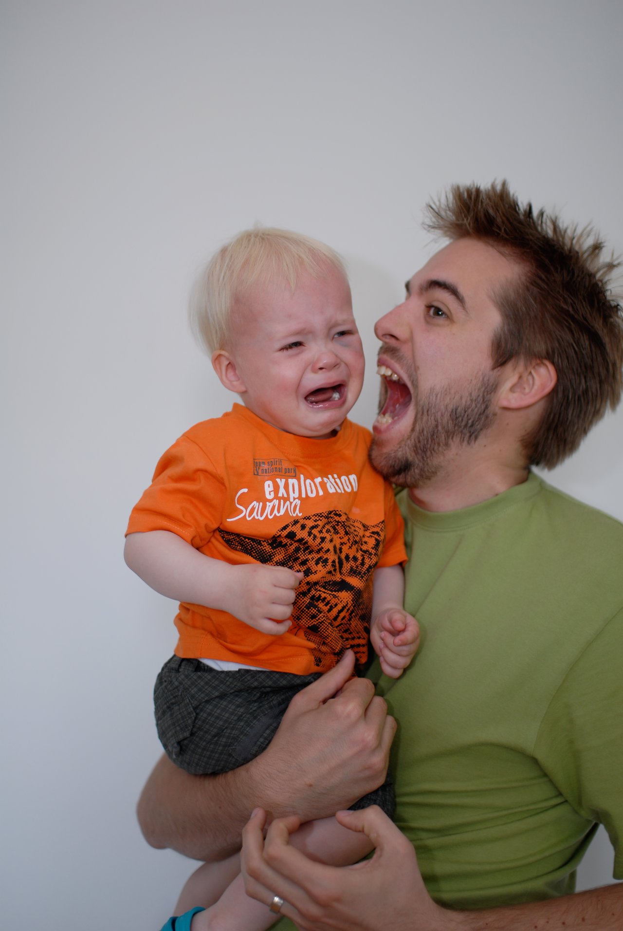 A man holds a crying toddler in his arms, looking at him with an open mouth.