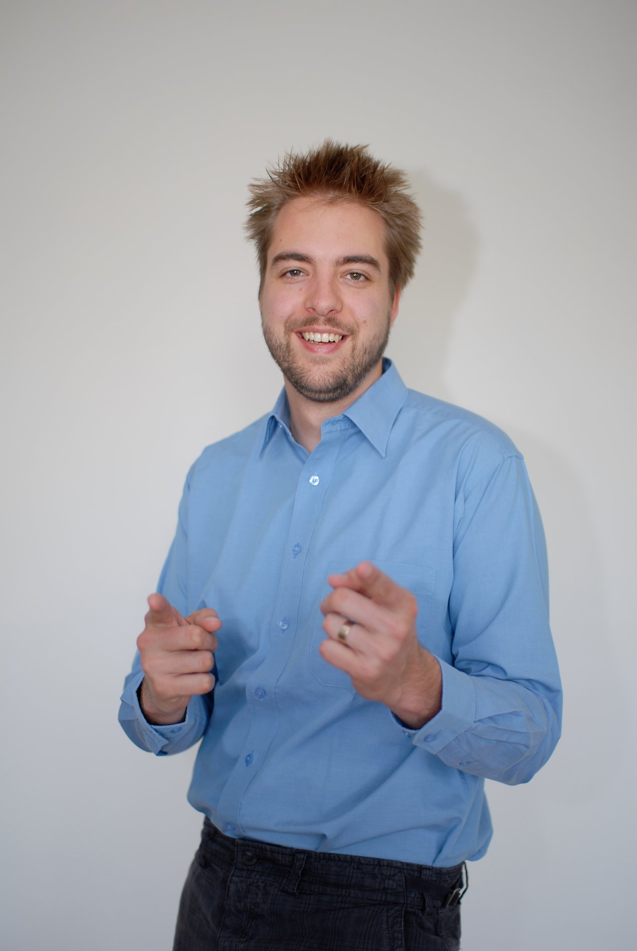 A man in a blue shirt smiles and points towards the camera with both hands.