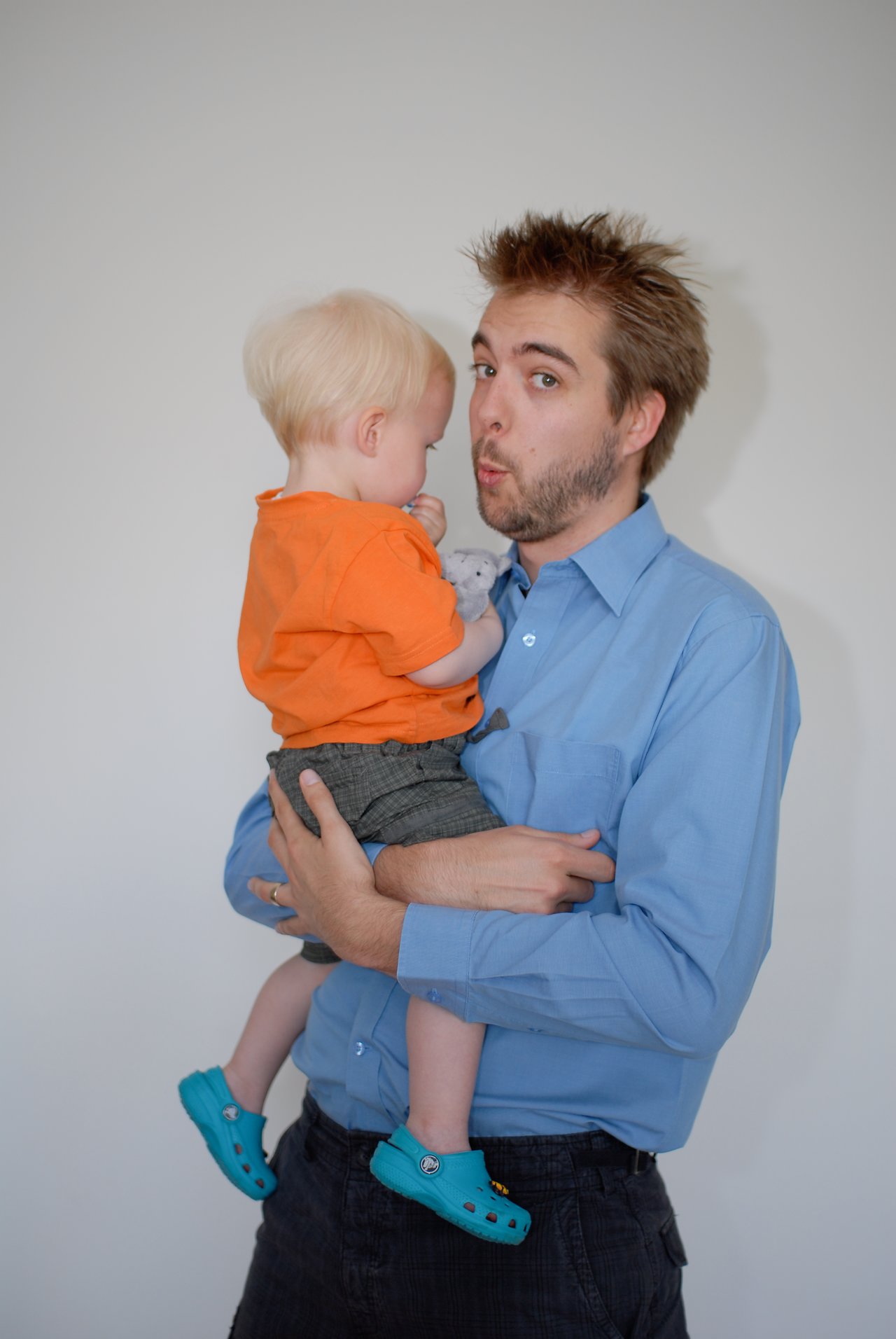 A man in a blue shirt holds a young child wearing an orange shirt and blue shoes.