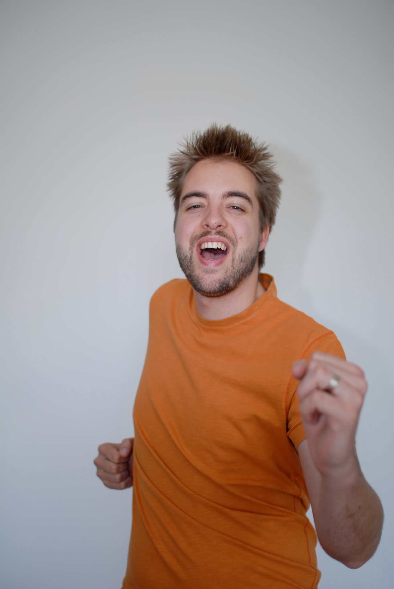 A man in an orange shirt smiles and moves energetically, appearing to be dancing or celebrating.
