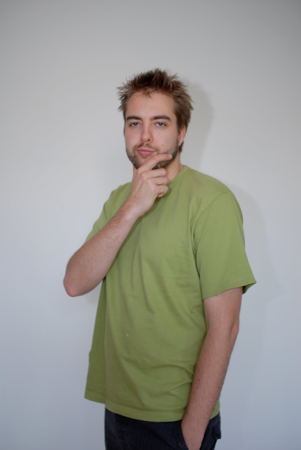 A man in a green shirt poses with his hand on his chin, looking thoughtful.