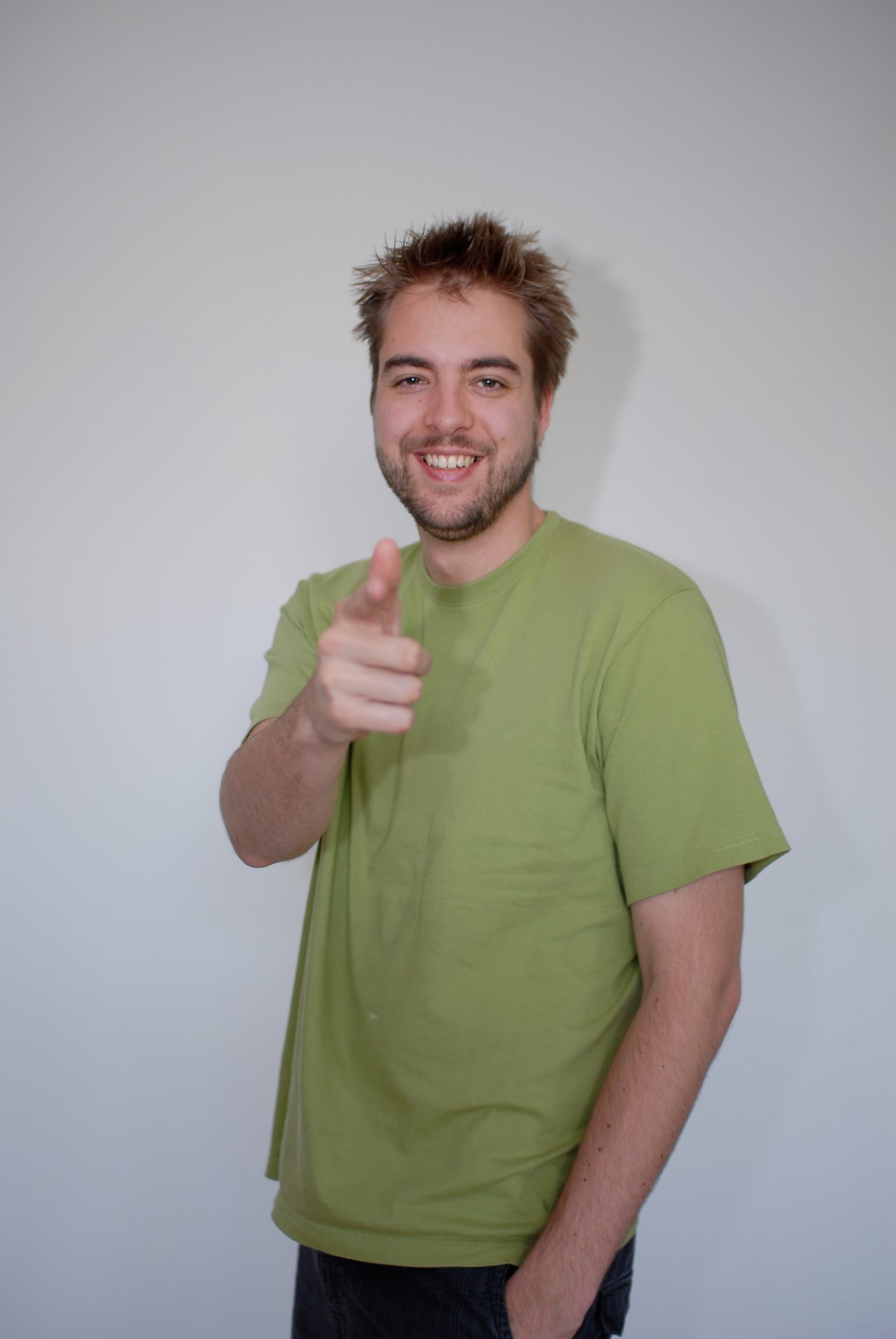 A man in a green shirt smiles and points toward the camera with one hand.