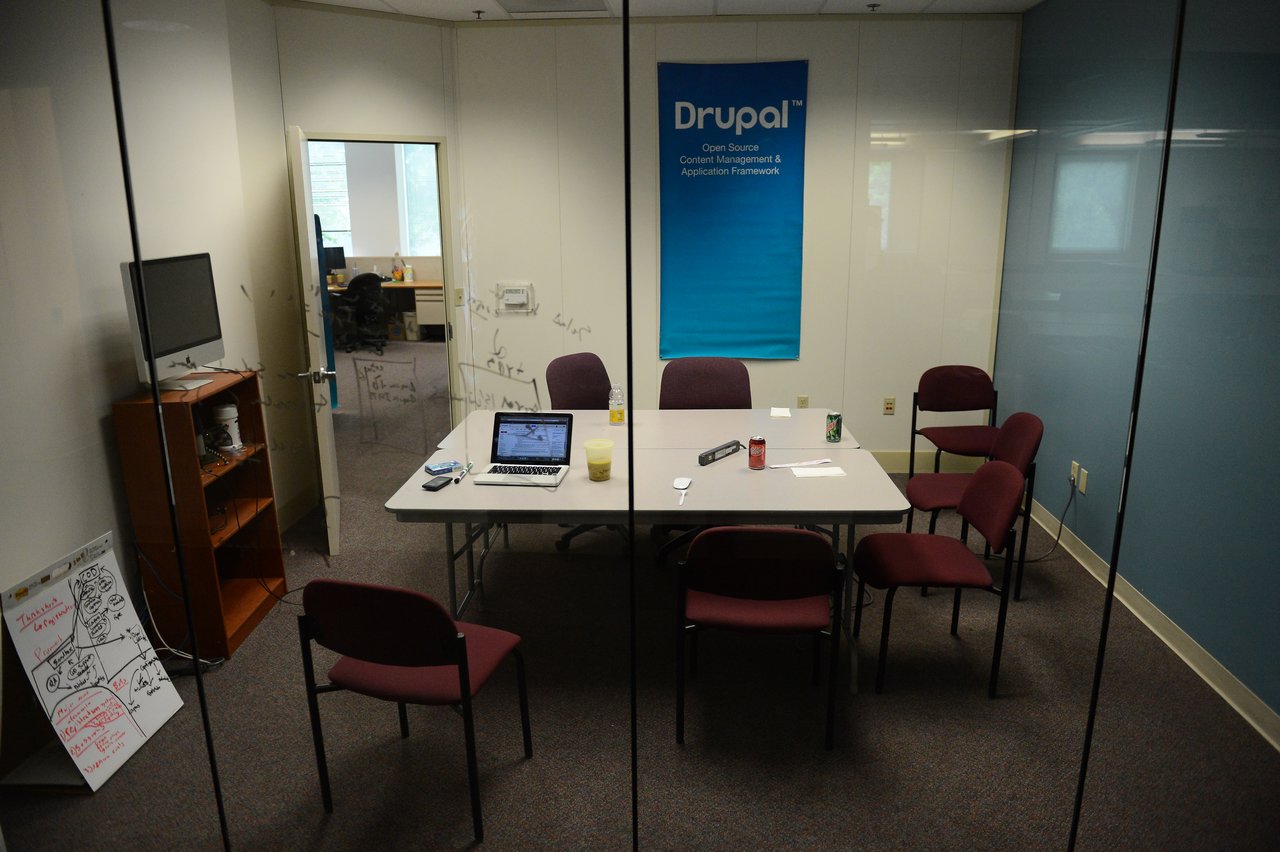 A conference room with a table, chairs, a laptop, and a Drupal banner on the wall.