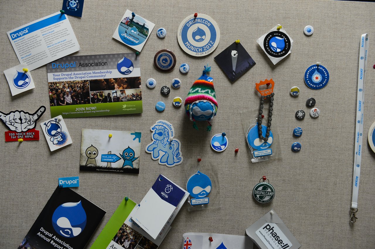 A bulletin board covered with Drupal-themed pins, badges, stickers, and memorabilia related to Drupal events and the community.